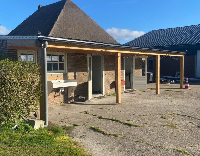 Het sanitairgebouw van Hoeve Voorwaarts overdag, met het rietgedekte boerderijdak op de achtergrond