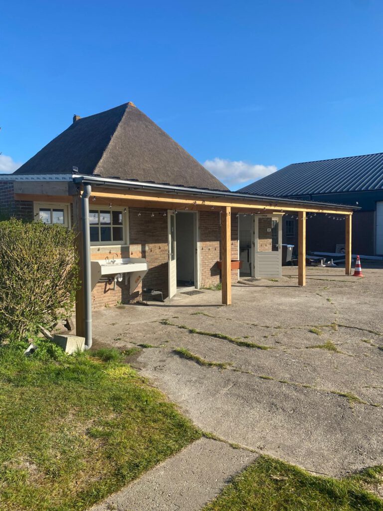 Het sanitairgebouw van Hoeve Voorwaarts overdag, met het rietgedekte boerderijdak op de achtergrond